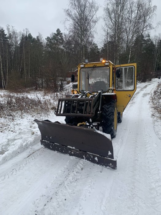 Gult bandfordon med plog framför på en snöig väg omgiven av vinterlandskap.