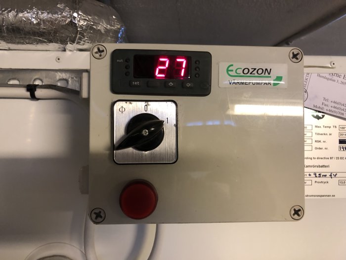 Värmepumpspanel med display som visar 27, strömbrytare i läge "on" och en röd stoppknapp.