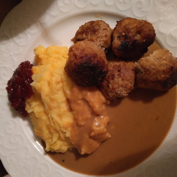 Ett fat med köttbullar, mosad potatis, lingonsylt och gräddsås.