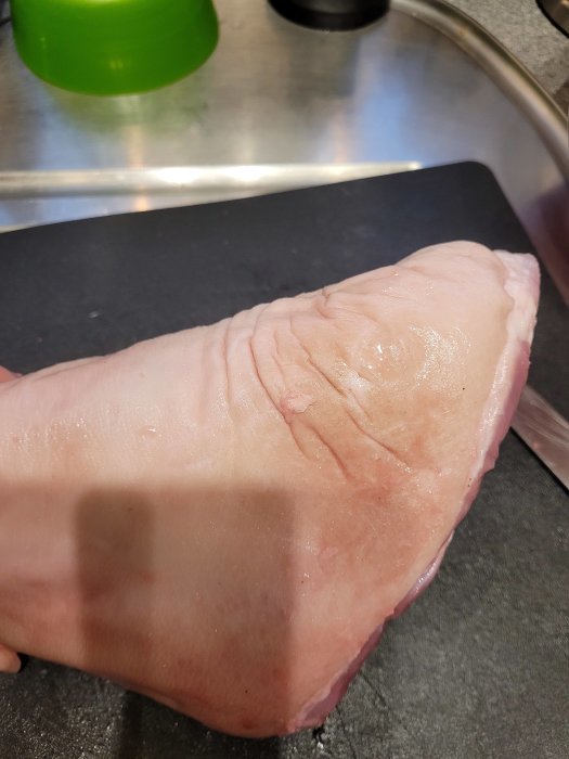 Rått köttstycke på en skärbräda nära en diskho med en skugga som faller över det.