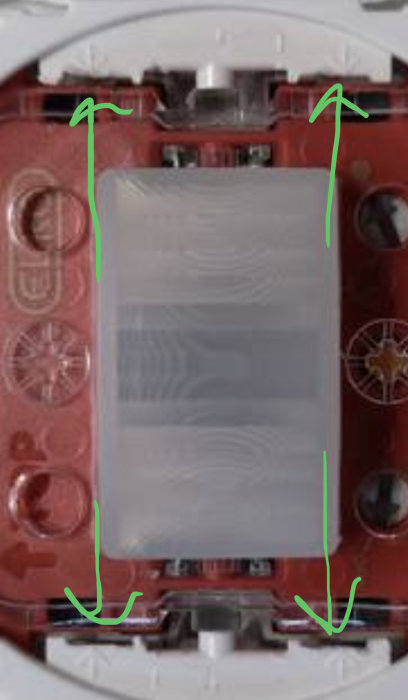 Elektrisk apparatdosa med grön markering som visar hur den vita sargen kan bändas från den röda basen.