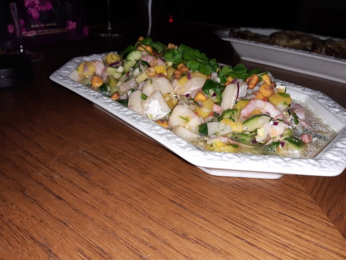 En tallrik med färgrik sallad med räkor, grönsaker och örter mot en mörk bakgrund.
