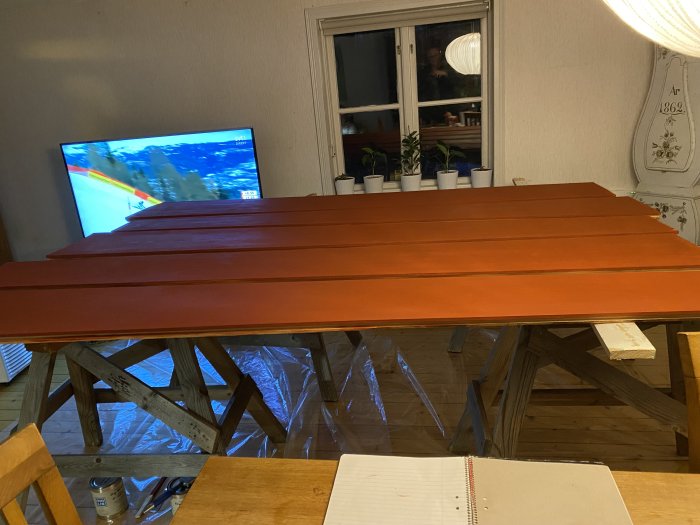 Ny målad röd dörr ligger på bockar för torkning i ett hem med en TV i bakgrunden.