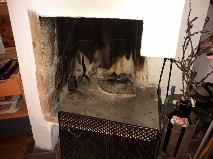 En öppen spis som behöver rengöras, med eldstadsgaller och sotfläckar på väggarna.