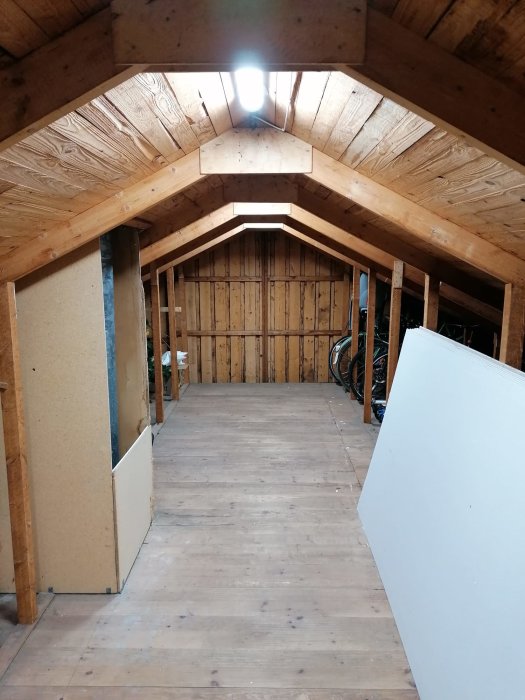 Oinredd vind med träkonstruktion och synliga takstolar, golvbrädor och stödpelare.