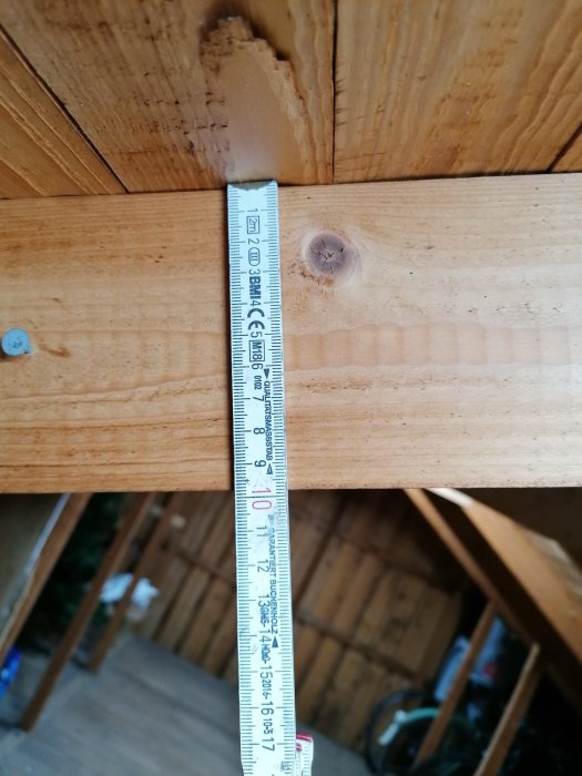 Måttband som visar 95 mm på en träregel under ett takstomme, inomhusmiljö.