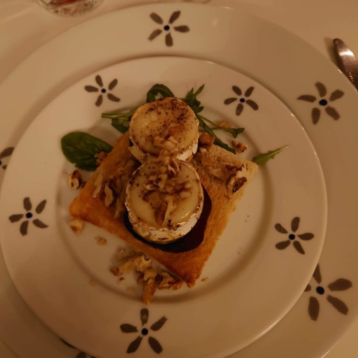 Förrätt med chevre på rödbeta och toast, dekorerad med valnötter på ett vitt blommönstrat fat.