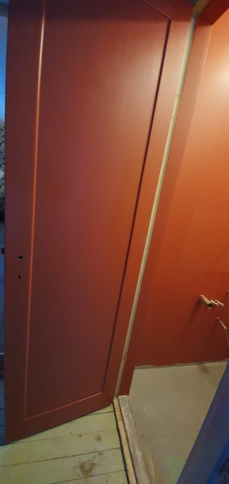 Röd skjutdörr med handtag i halvfärdig rumsvinkel, synliga rör och oavslutat golv.