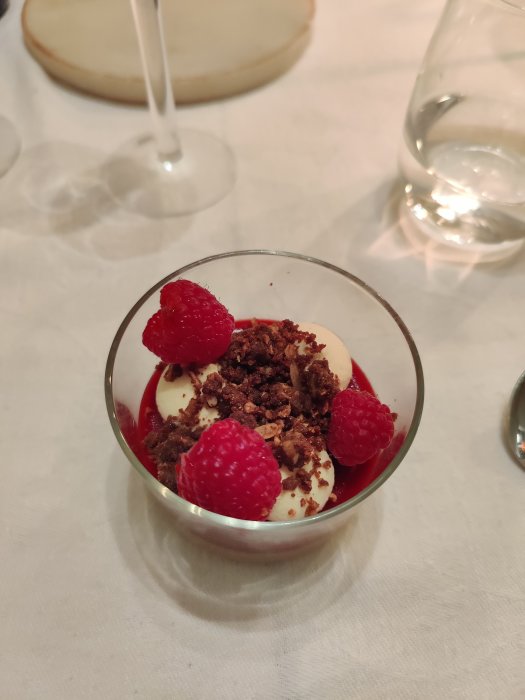 Chokladmousse med hallonspegel toppad med färska hallon och kaksmulor i ett glas.