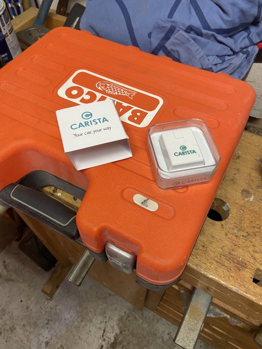 En uppsättning Carista bilverktyg med en smartphone adapter på ett orange verktygskoffert.