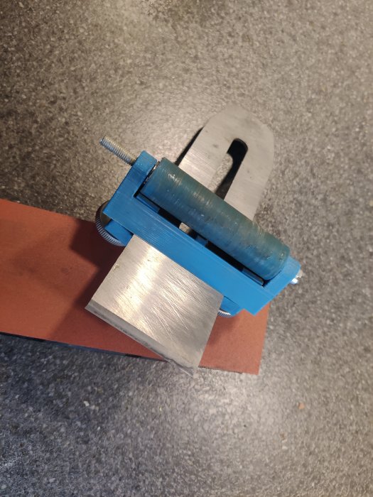 En 3D-utskriven blå jigg håller fast ett metallhyvelblad för slipning på en brun slipsten.