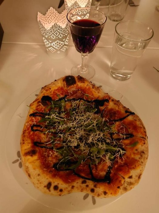 Hemmagjord pizza med prosciutto, ruccola och riven ost serveras med rött vin och vatten.