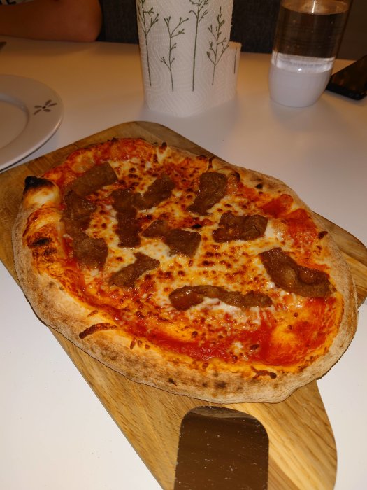 Hemgjord kebabpizza på skärbräda med synlig luftbubblor i kanterna och topping med kebabkött.