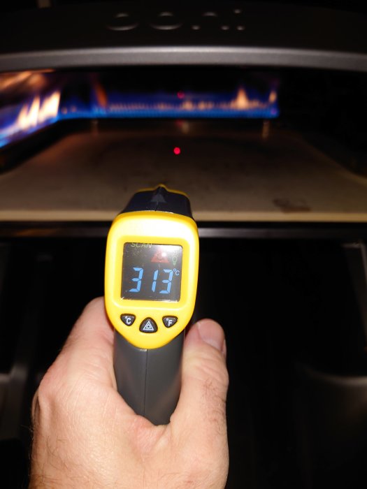 Infraröd termometer visar 313°C framför en igång pizzaugn.
