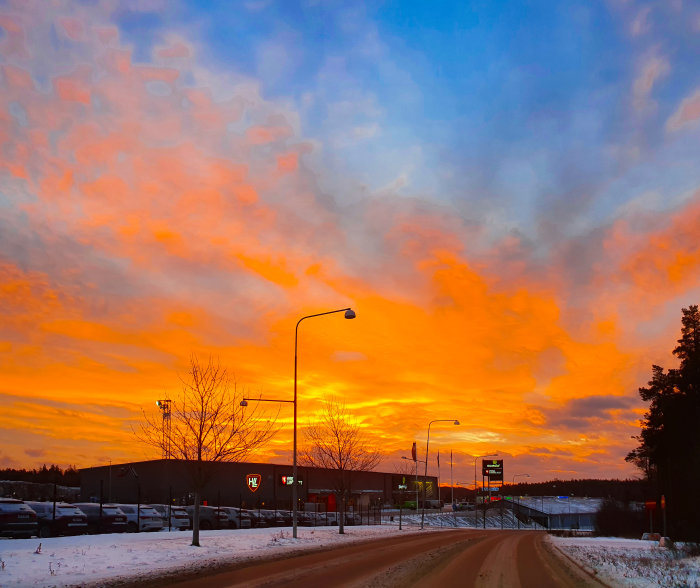 Vintergata med dramatisk solnedgång i orange och blå toner över en snöbeklädd stadsscen.