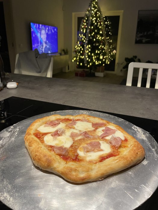 Hemlagad pizza på serveringsfat med julgran med belysning i bakgrunden och oskarp TV.