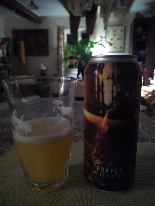 Ölburk från Spartacus Brewing med etikett "Prayer", bredvid ett glas med skummande öl i ett rumsinteriör.