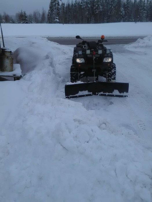 Fyrhjuling med mittmonterat snöblad i användning, röjer snö vid vägkant.