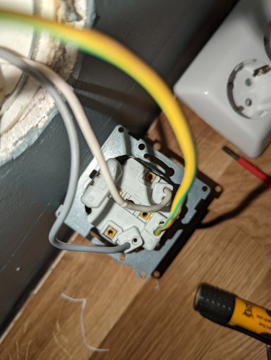 Eluttag utan anslutningar med vita och gråa kablar, intill ett monterat vägguttag.