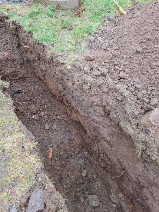 Grävd grå för anslutning av utbudggnad till trekammarbrunn med synliga jordlager och stenar.