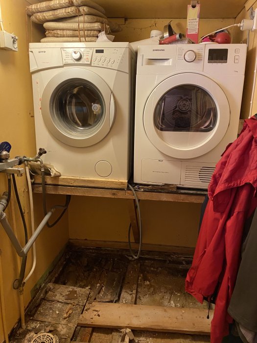 Tvättmaskin och torktumlare på trähylla, söndertagna väggfasta hyllor och ho, skadat golv.