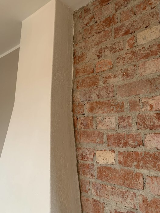 Övergång mellan en ojämn putsad vägg och en rå tegelvägg.
