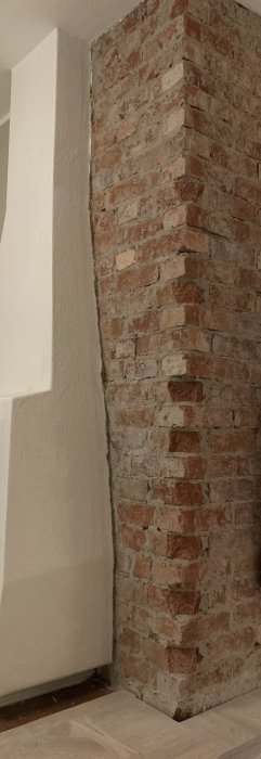 Ej jämn övergång mellan en vitputsad vägg och exponerat tegel i ett hörn.