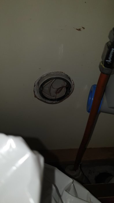 Öppning i vägg under vask med oskyddade elkablar och rörinstallationer.