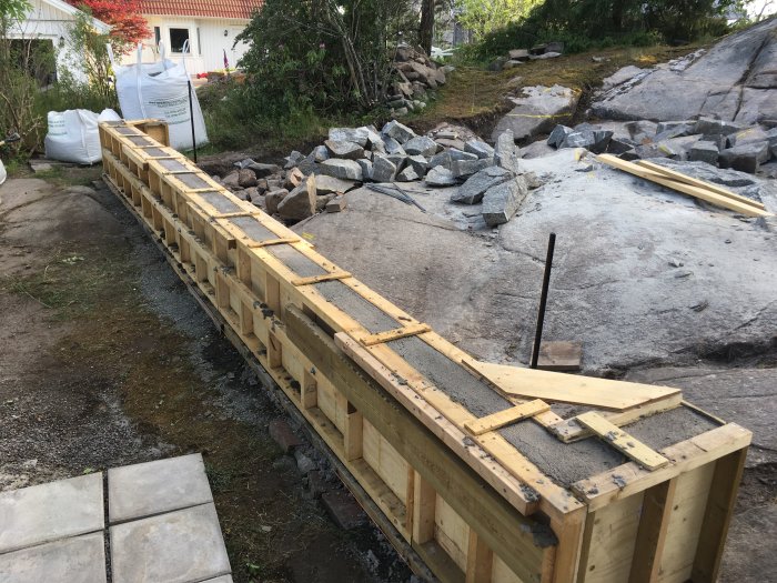 Gjutform för stödmur med armerad sula på byggplats med granitunderlag.