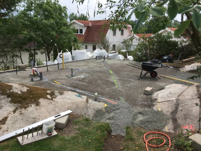 Grundarbetsplats för Attefallshus med märkta rörledningar, grus och byggmaterial på en rymlig tomt.