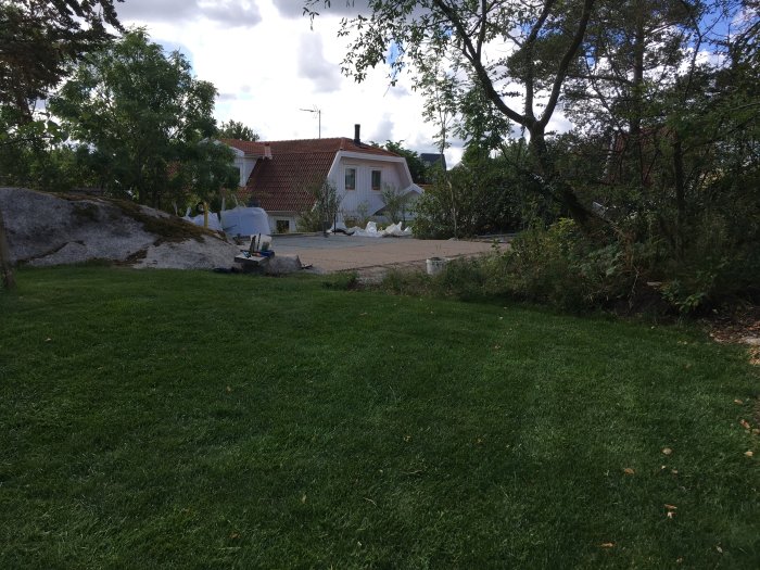 Trädgårdstomt i utkanten av Göteborg med gräsmatta, granithäll och byggmaterial för grunden till ett Attefallshus.