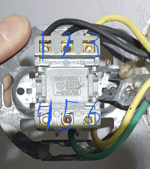 Hand som håller en elektrisk brytare med märkta skruvanslutningar numrerade 1 till 6.