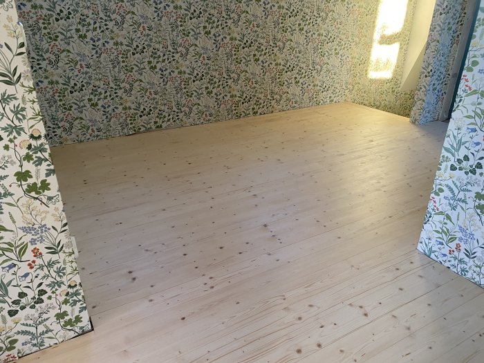 Nybehandlat ljusare trägolv i ett rum med blommigt tapetserade väggar.