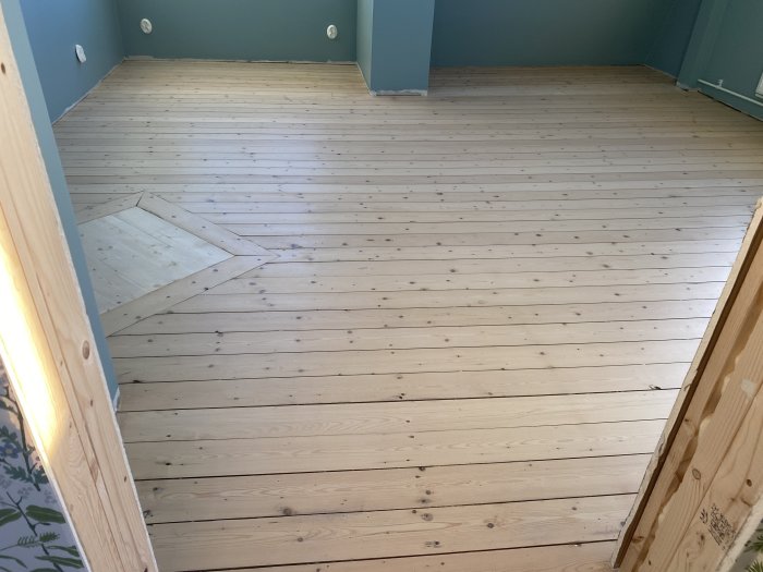 En nyslipad ljust trägolv med en inbyggd fyrkantig matta av trä vid ingången.