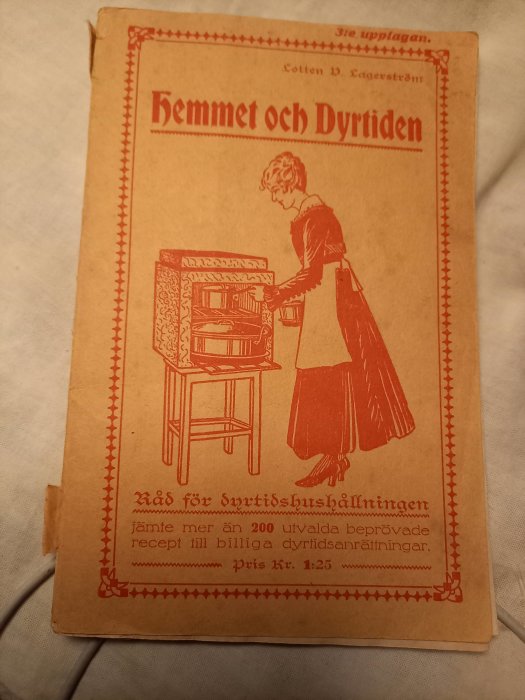 Gammalt häfte från 1917 med titeln "Hemmet och Dyrtiden", kvinna vid skrivbord.