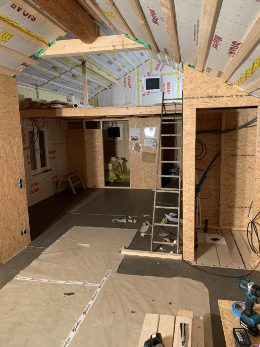 Interiör av ett pågående byggprojekt med synliga bjälkar och OSB-skivor.