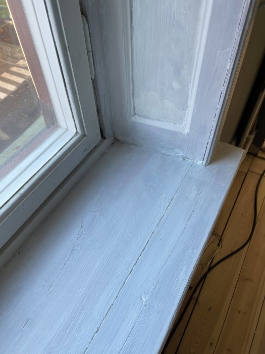 En del av ett gammalt fönster i en sekelskifteslägenhet där lös färg avlägsnats och ytan slipats inför renovering.