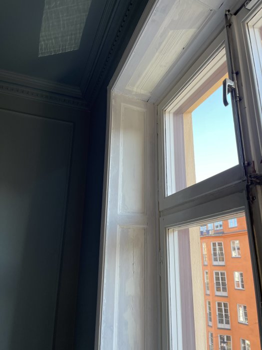 Sekelskiftesfönster under renovering, med borttagen färg och slipade ytor, mot bakgrund av stadsbebyggelse.