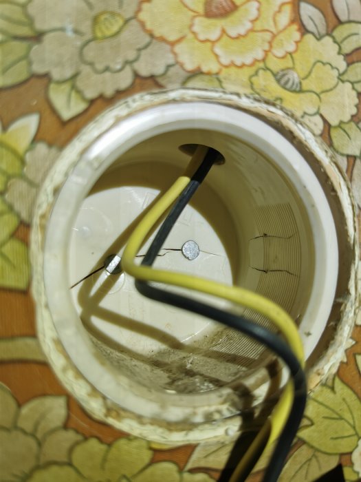 Trasig plastdosa med elledningar i ett äldre hus, spikad i bakkant, behov av reparation eller utbyte.