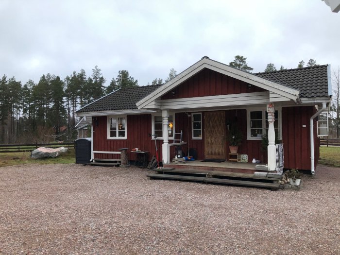 Rött trähus med veranda och grusuppfart under molnig himmel.