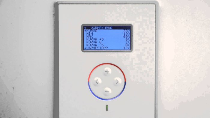 Digital termostat med inställd värmevärdet och justeringsknappar på en vit vägg.