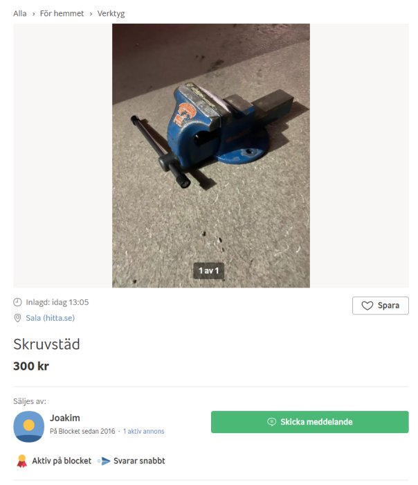 Blå skruvstäd på betonggolv med öppna käftar och en inspänd svart skruv.