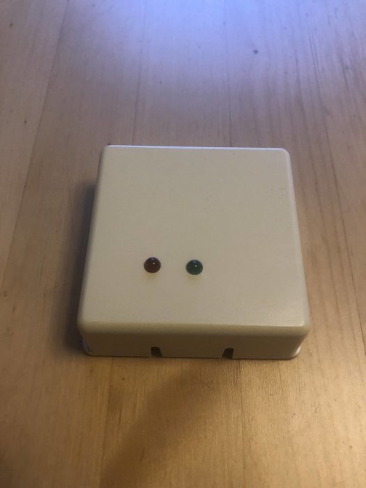 Gammal rumsgivare i elfenbensvitt med två färgade indikatorlampor på en träyta.