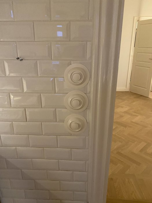 Vit kakelvägg med runda dimmers och tapetskydd, döljer kapade plattor, nära ett dörröppning.