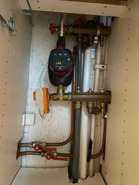 Installation av VVS med rör, ventiler och mätare i ett vitmålat skåp.