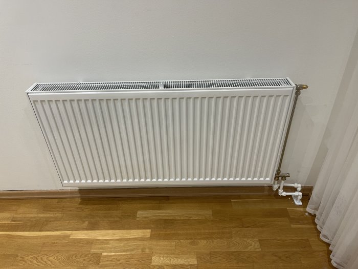 Väggmonterat radiatorselement i ett rum med parkettgolv och vita väggar.