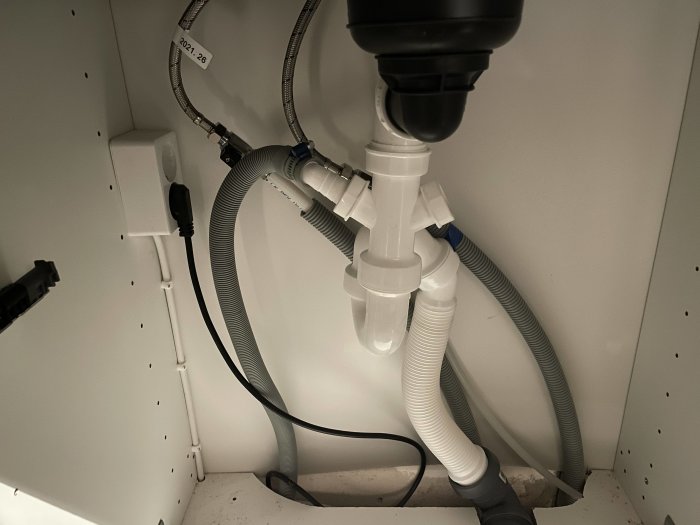 Installation under diskbänk med avstängningsventiler, avloppsrör och diskmaskinsavlopp liggandes på golvet.