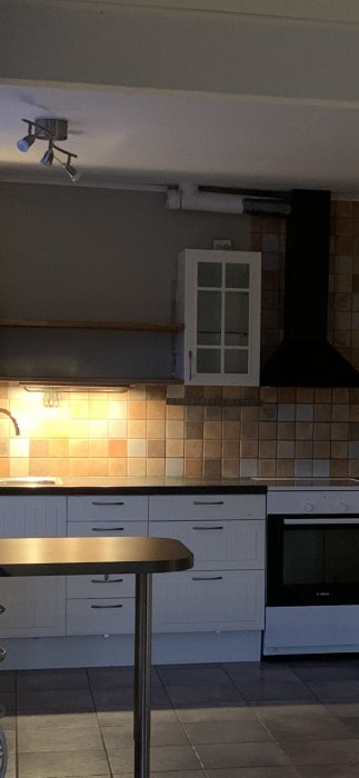 Kök med omålat kakel ovanför vita skåp och svart spishäll, fråga om målning.