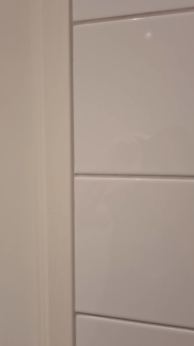 Renoverat badrum med kaklade väggar och nyinstallerat dörrfoder, detaljbild av fogar och hörn.