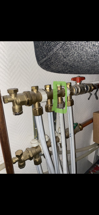 VVS-installation med flera vita rör och mässingsventiler, en ventil markerad med grönt.